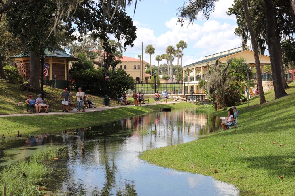 several groups of people sitting in a park with a creek running by