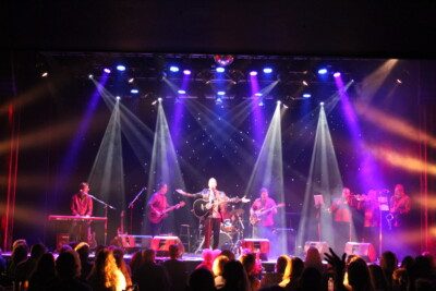 Man performing on stage with a band behind him.