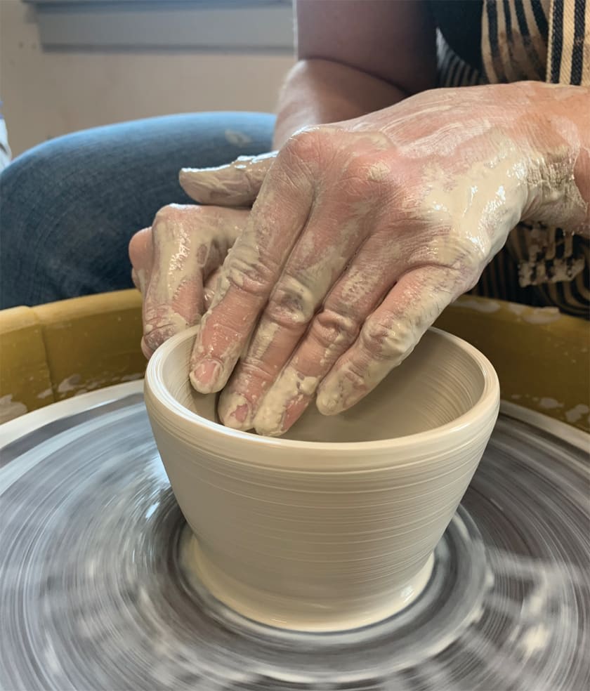 Person using a pottery wheel to create a bowl.