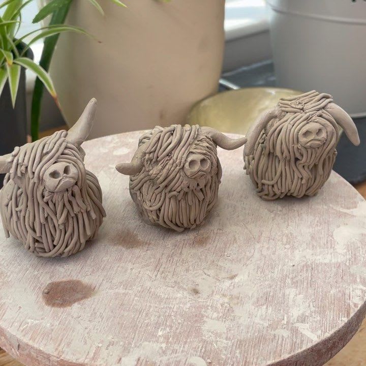 Three small sculptures of highland cows on a table.