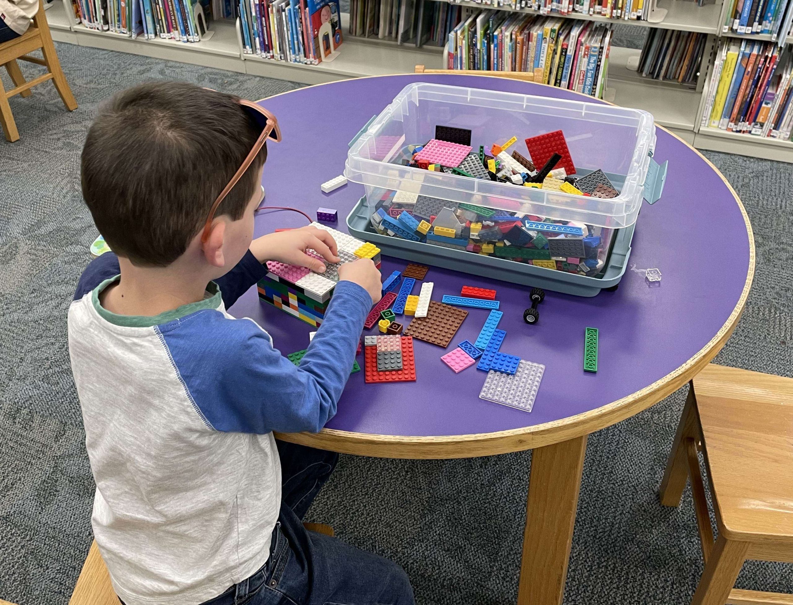 Photo of a boy sitting at a table playing with multicolored LEGOs