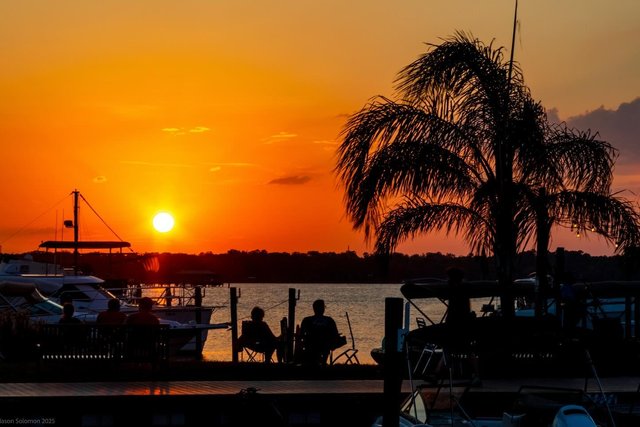 Sunset with silhouettes of boats and people hanging out by the water at Sunset Tiki Bar