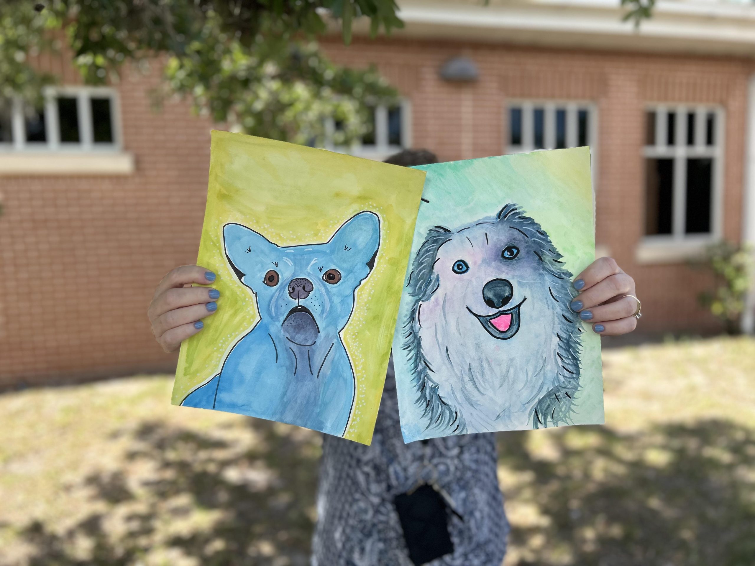 Person holding two water color portraits of dogs.
