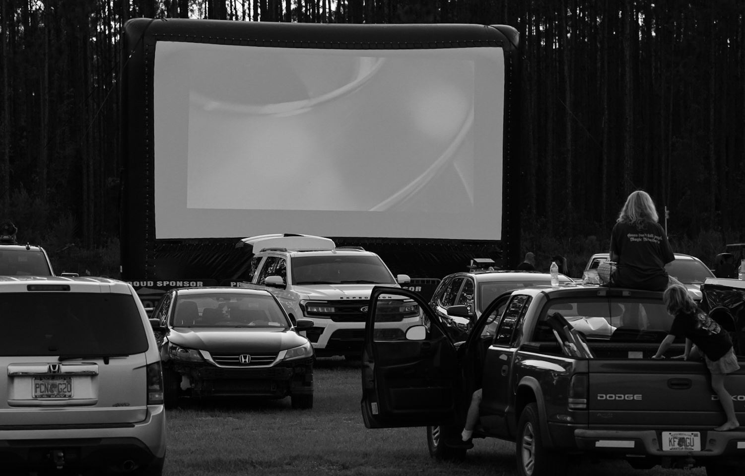 Black and white photo of cars parked in front of a movie screen.